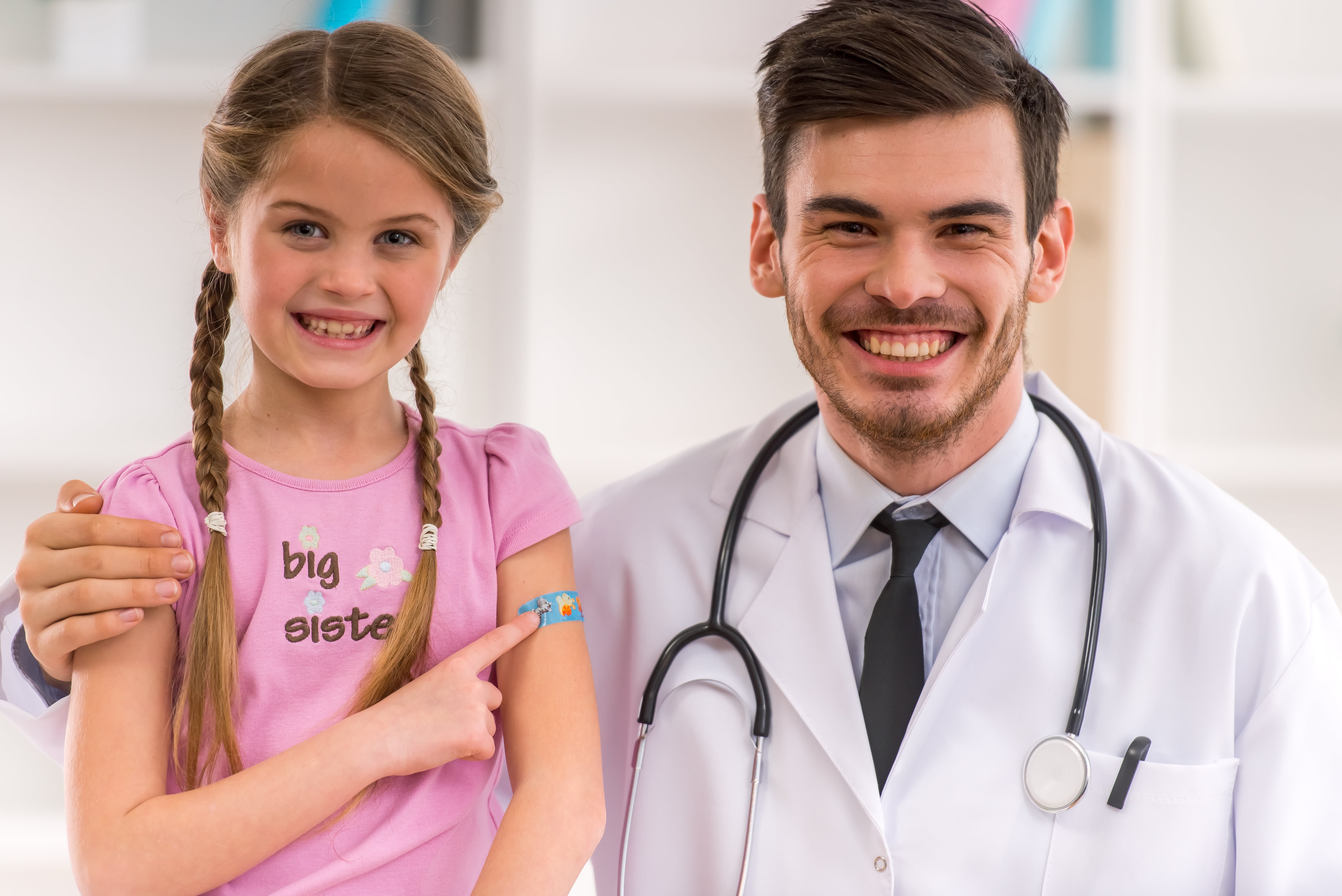 a smiling girl with a bandaid standing next to a smiling doctor